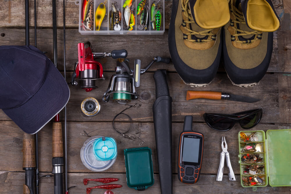 foto com diversos equipamentos de pesca: molinetes, varas, iscas, linha, gps, alicate, botas e boné